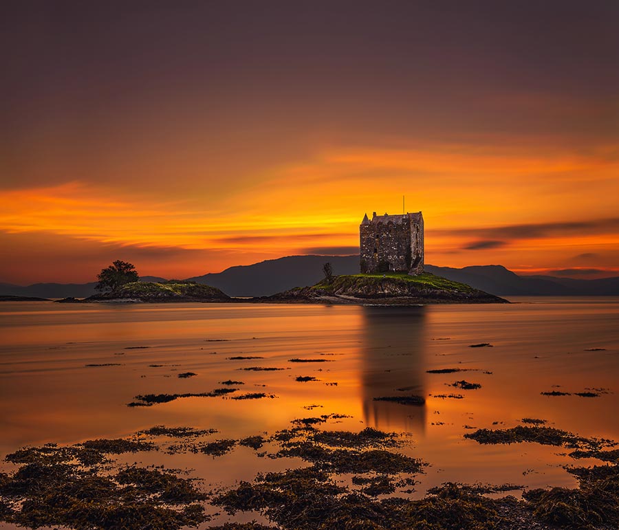 Dramatic sunset over Castle Stalker with reflection in Loch Appin located in Scotland, United Kingdom. Long exposure and hdr processed.